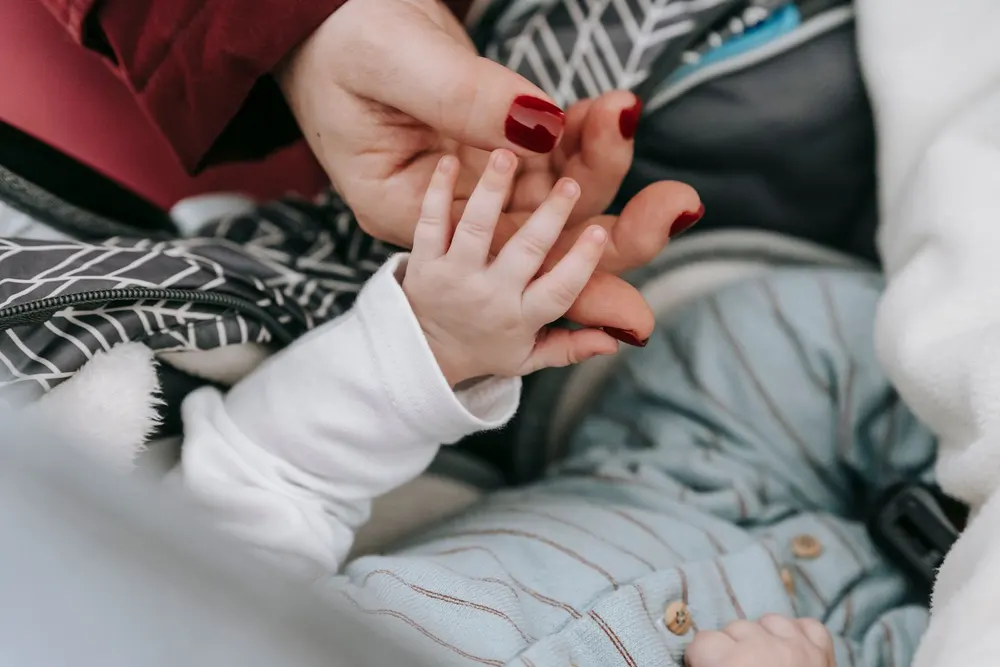 A mother holding her newborn baby's hands on a soft blanket